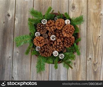 Top view of a Christmas basket filled with pine tree branches, cones on rustic wooden boards.