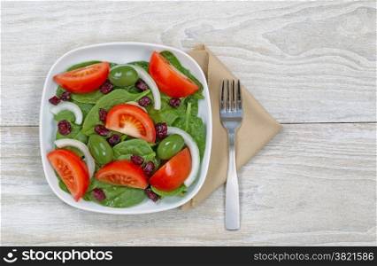 Top view of a freshly made salad in white plate and fork with cloth napkin on rustic white wood ready to eat