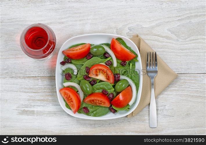 Top view of a freshly made salad, in white plate, glass of red wine and fork with cloth napkin on rustic white wood ready to eat