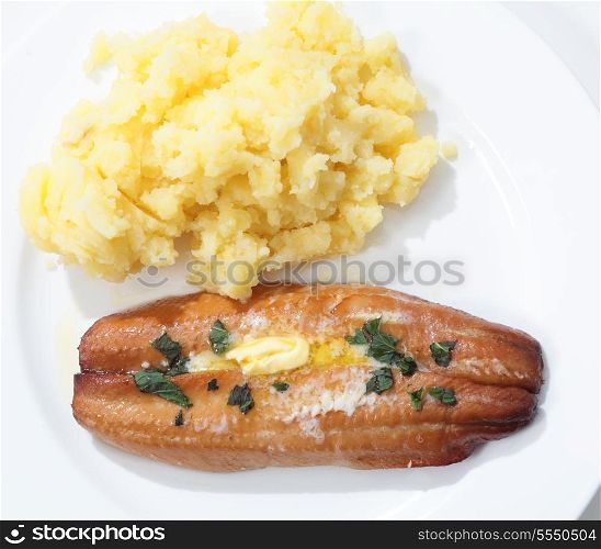 Top view of a grilled kipper (smoked herring) garnished with butter and herbs on a plate with mashed potato.