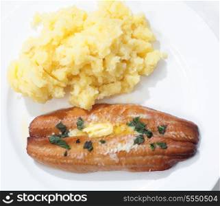 Top view of a grilled kipper (smoked herring) garnished with butter and herbs on a plate with mashed potato.