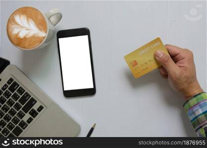 top view of a man holding a credit card Mobile phone mock up blank white screen and computer and coffee Business communication technology, online shopping concept.