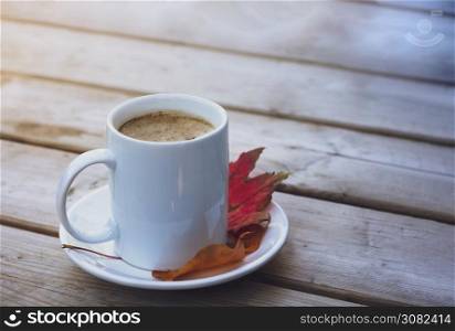 Top view of a mug coffee latte with foam on wooden table, Hot coffee in white cup with red and yellow leaves on wooden table, Hot drink for Autumn background