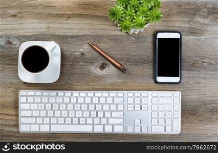 Top view of a neat desktop with keyboard, black coffee, green plant and cell phone on wooden desk.
