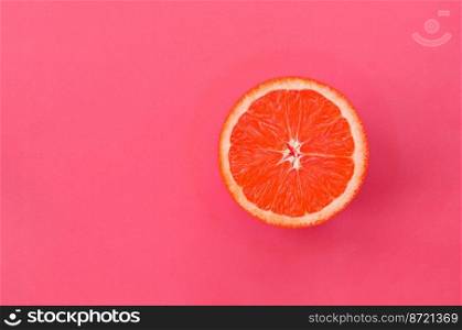 Top view of a one grapefruit slice on bright background in light pink color. A saturated citrus texture image