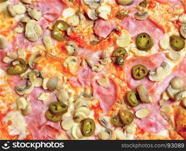 Top view of a pizza with chili peppers, ham and mushrooms.