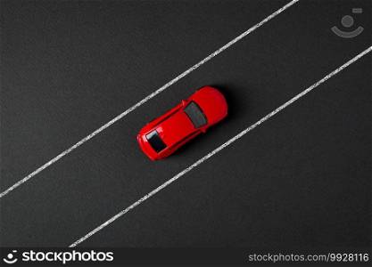 Top view of a red toy car driving on the drawn road line on a gray background
