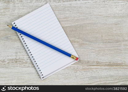 Top view of a used office wooden white desktop with small notepad and sharpen blue pencil