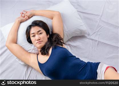 Top view of a young attractive asian woman stretching hands while lying in bed in the morning.