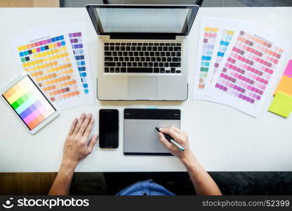 Top view of a young graphic designer working on a desktop computer and using some color swatches, top view.