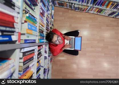 top view of a young student with glasses sits in the library, reads a book and makes notes with a latpop