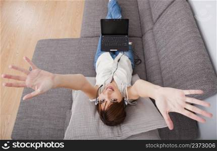 Top view of a young woman at home with arms open and with a laptop.