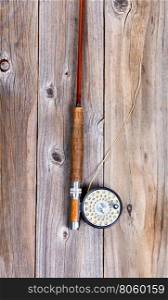 Top view of antique fly rod and reel on rustic wooden boards in vertical layout.