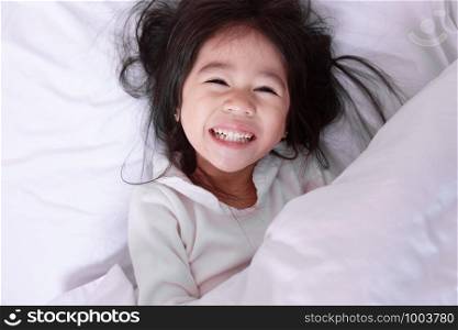 Top view of Asia little kid having fun lying on a bed in the morning on soft pillows laughing feels happy.