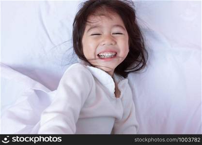 Top view of Asia little kid having fun lying on a bed in the morning on soft pillows laughing feels happy.