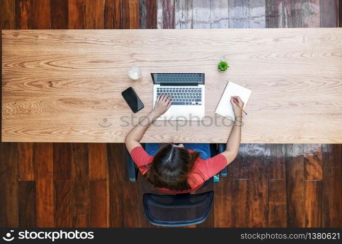 Top view of Asian business woman using technology laptop and writing notebook for working from home in outdoor home and garden, startups and business owner, social distance and self responsibility