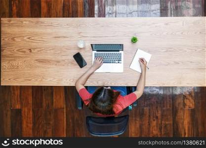Top view of Asian business woman using technology laptop and writing notebook for working from home in outdoor home and garden, startups and business owner, social distance and self responsibility