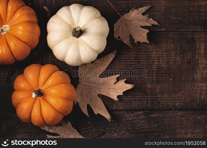 Top view of autumn leaves and mini pumpkins on wooden background