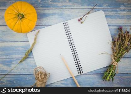 Top view of autumn orange pumpkins and dry flowers with grass thanksgiving background over blue toned wooden table with notebook mock up and copy space in rustic style, template for text