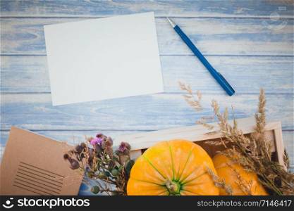 Top view of autumn orange pumpkins and dry flowers with grass thanksgiving background over blue toned wooden table with blank letter mock up and copy space in rustic style, template for text