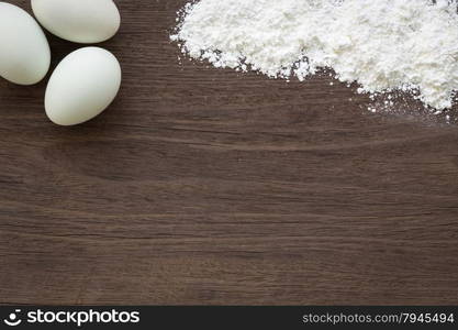 Top view of baking background with eggs and flour on vintage natural wood table. Rough texture and rustic surface with blank space for text.