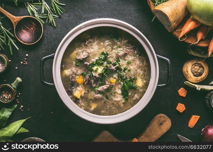 Top view of beef and cabbage soup or stew in cast iron cooking pot on dark background with ingredients and wooden spoon, top view. Healthy clean low-calorie food and eating concept