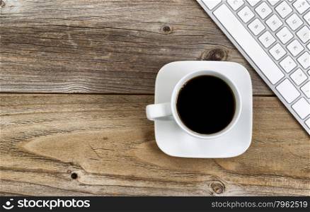 Top view of black coffee, selective focus on upper lip of coffee cup, with partial computer keyboard on rustic wood.