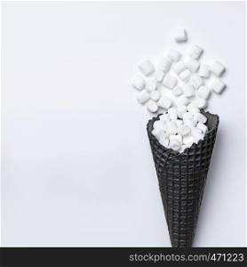Top view of black waffle cone with marshmallows on white background, flat lay