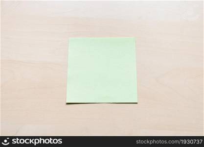 top view of blank green sheet of note paper on light brown wooden board