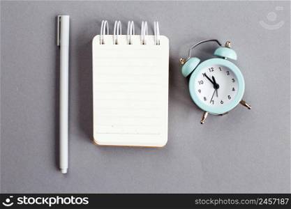 Top view of blank note paper with pen and alarm clock on gray background.. Top view of blank note paper with pen and alarm clock on gray background