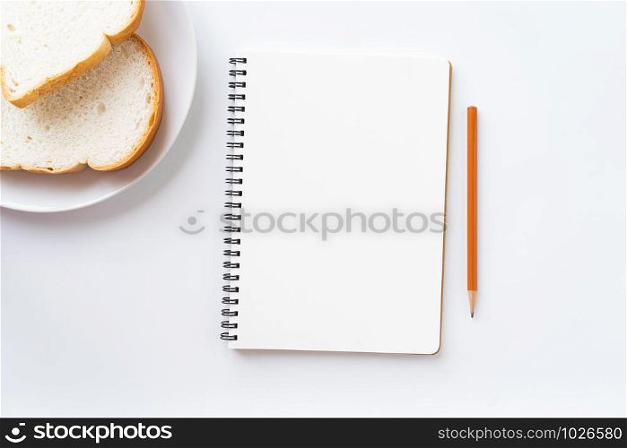 Top view of blank notebook on the table. bread in a plate and pencil on a white ground