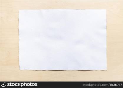 top view of blank sheet of white textured watercolour paper on light brown wooden board