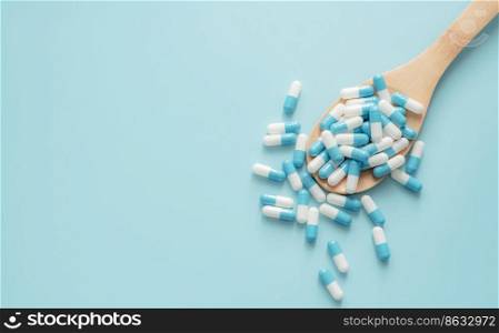 Top view of blue-white antibiotic capsule pills on wooden spoon and blue background. Antibiotic drug resistance. Prescription drug. Medical care. Pharmaceutical care. Antimicrobial drug overuse.