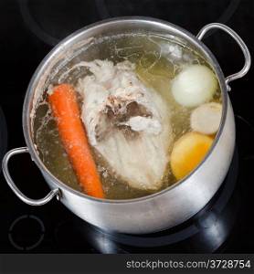 top view of boiling chicken broth with seasoning vegetables in steel pan on glass ceramic cooker