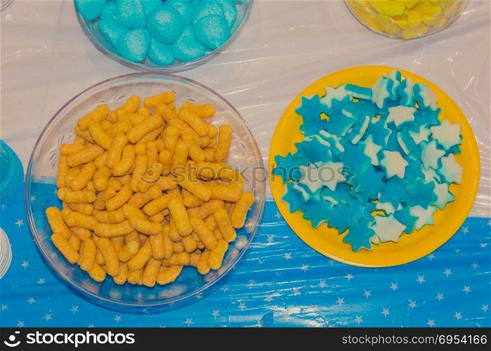 Top view of bowls with colorful sweet tasty gummy candy and bamba snack at children birthday party.