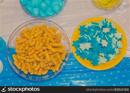 Top view of bowls with colorful sweet tasty gummy candy and bamba snack at children birthday party.