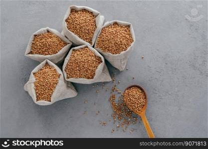 Top view of brown buckwheat in sacks and wooden spoon over grey background. Healthy diet concept. Buckwheat groats. Biologically grown organic plant