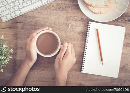 Top view of business hand on desk have coffee, toast, notebook blank and pencil on wooden table background. Picture of the home office concept.