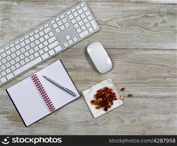 Top view of business office consisting of computer keyboard, notepad, pen, and snack food on rustic white wooden desktop