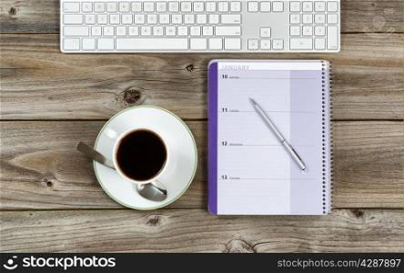 Top view of business office objects consisting of calendar, pen, computer keyboard and cup of coffee on rustic wooden desktop