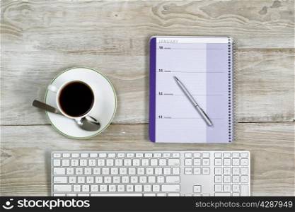 Top view of business office objects consisting of calendar, pen, computer keyboard and cup of coffee on white wooden desktop