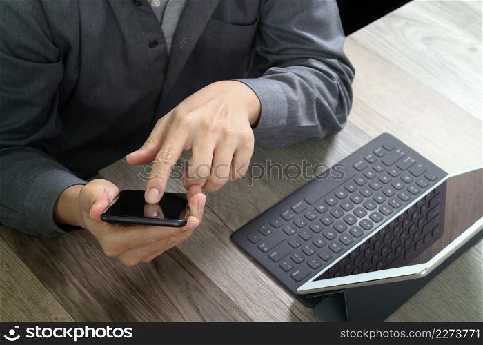top view of businessman hand using smart phone,mobile payments online shopping,omni channel,digital tablet docking keyboard computer in modern office on wooden desk