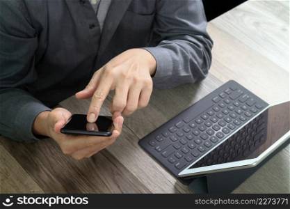 top view of businessman hand using smart phone,mobile payments online shopping,omni channel,digital tablet docking keyboard computer in modern office on wooden desk