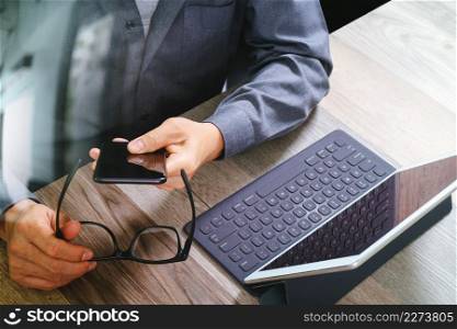 top view of businessman hand using smart phone,mobile payments online shopping,omni channel,digital tablet docking keyboard computer,eyeglasses,in modern office on wooden desk,filter