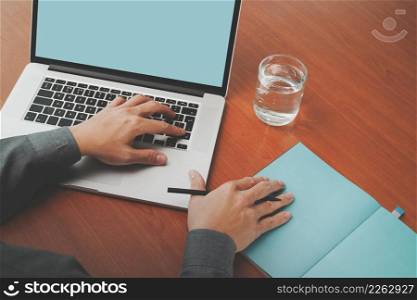top view of businessman hand working with new modern blank screen computer on blank book on wooden desk as concept