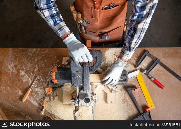 Top view of carpenter holding plank near circular saw in carpentry shop. High quality photo.. Top view of carpenter holding plank near circular saw in carpentry shop