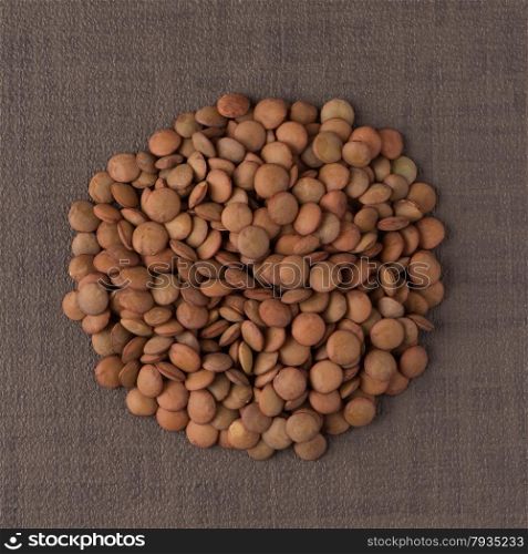 Top view of circle of lentils against brown vinyl background.