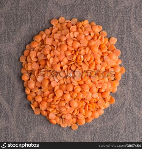 Top view of circle of peeled lentils against brown vinyl background.