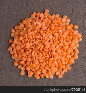 Top view of circle of peeled lentils against brown vinyl background.