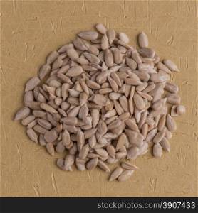 Top view of circle of shelled sunflower seeds against brown vinyl background.